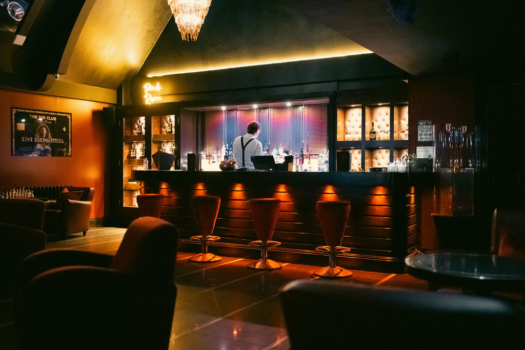 The bar, lit in amber, with velvet bar stools